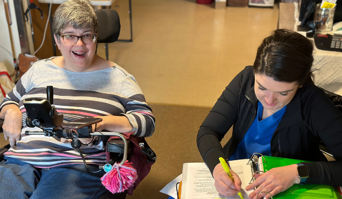 Woman in a power wheelchair smiling while Lindsey Morris writes